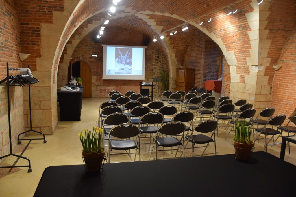 Aménagement de la grande salle voûté du château pour un séminaire ou une conférence, avec des chaises et un rétro-projecteur