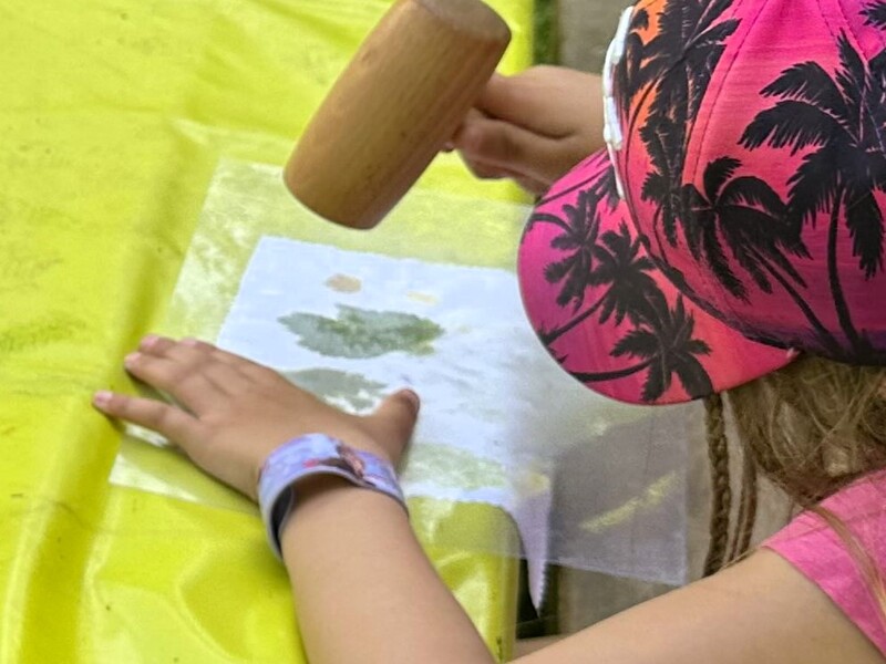 photo d'un enfant en train de taper sur une feuille avec un petit maillet, pour l'imprimer sur le tissu en dessous